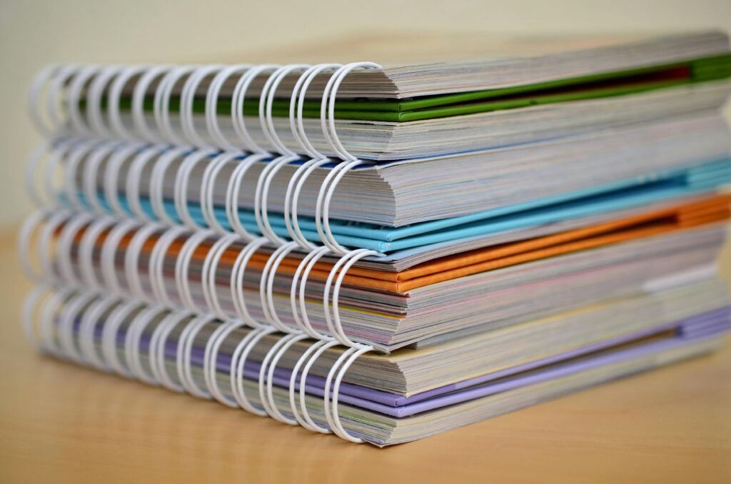 pexels-photo-272980-272980 A colorful stack of spiral-bound notebooks neatly placed on a wooden desk. Ideal for educational themes.